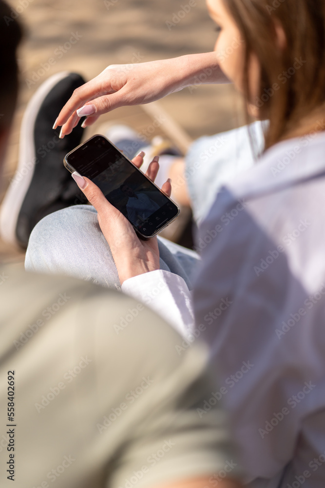 Young couple watching online content in a smart phone sitting on a bench in the park