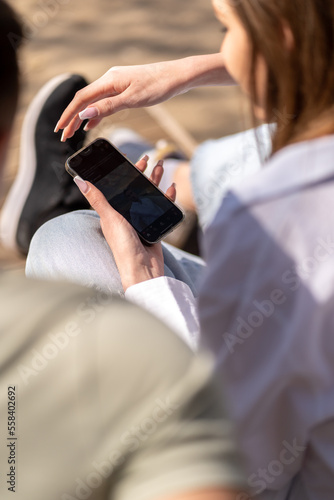 Young couple watching online content in a smart phone sitting on a bench in the park
