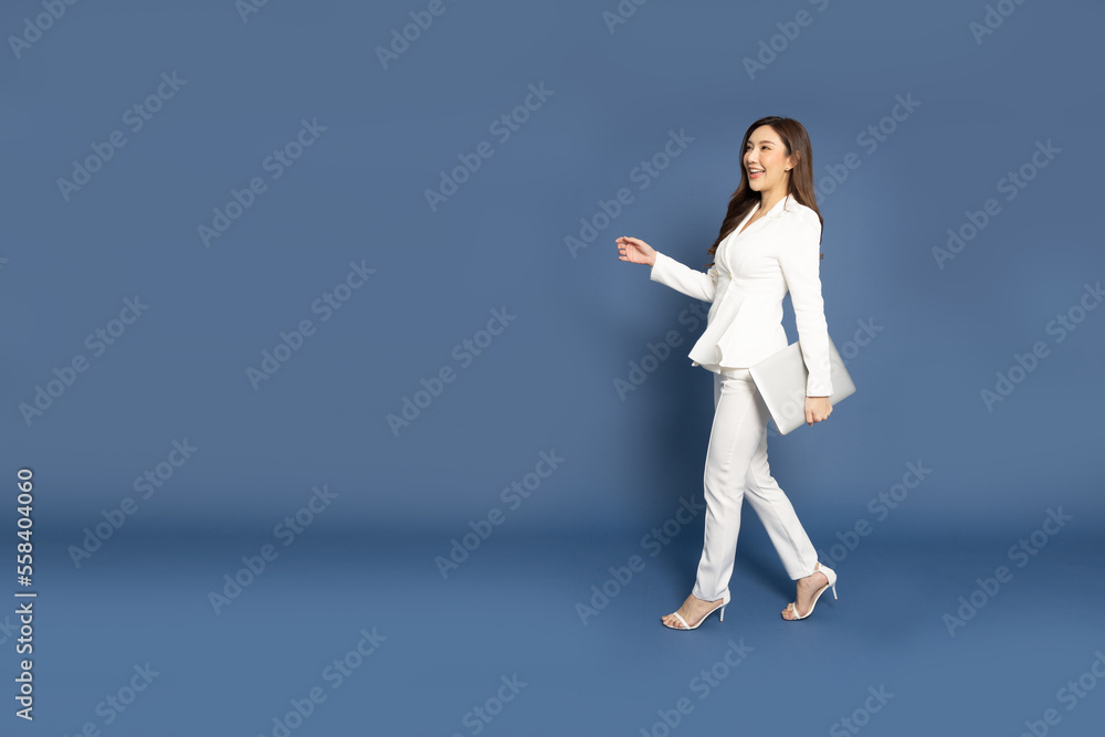 Happy Asian businesswoman walking and holding laptop computer over blue background