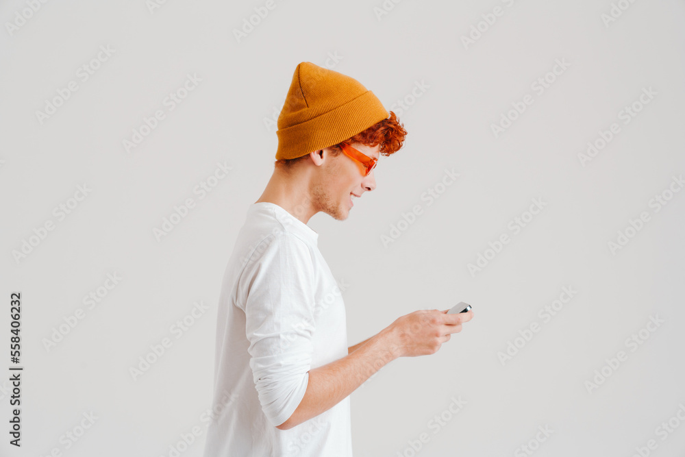 Young ginger smiling man wearing sunglasses using mobile phone
