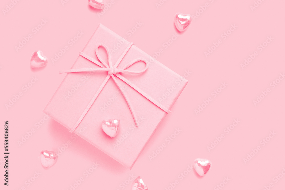 Pink gift box with bow on pink background with hearts decoration around