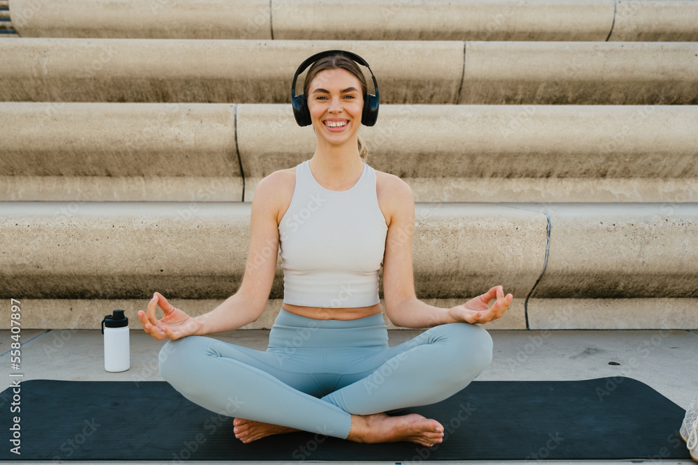 Young joyful woman in sportswear sitting in lotus pose outdoors at city street Young joyful woman in sportswear sitting in lotus pose outdoors at city street