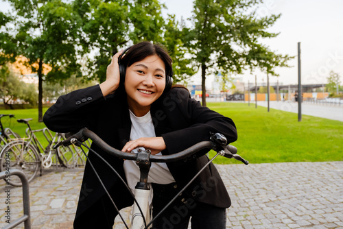 Young asian woman using headphones while riding bicycle in city park