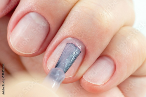 Young Caucasian woman making self manicure at home with the help of shellac gel polish and other tools for nail procedures.