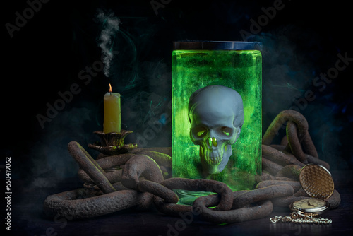 Glowing magic skull in a jar on a wooden table chained. Smoke comes from a candle, an old clock has stopped time. photo