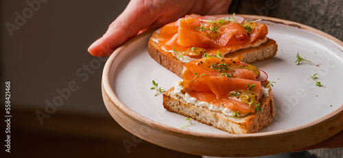 close up of woman holding white plate with smoked salmon toast as fresh snack, day light. Clean Eating. Healthy breakfast.