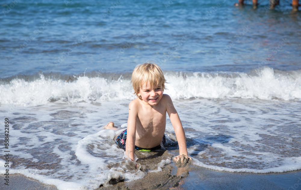 Fototapeta premium happy cheerful child, boy 4-5 years old, lying in sea water on coast. kid has fun on hot summer day, cooling off in the sea. concept of healthy lifestyle and recreation. Happy childhood, hello summer
