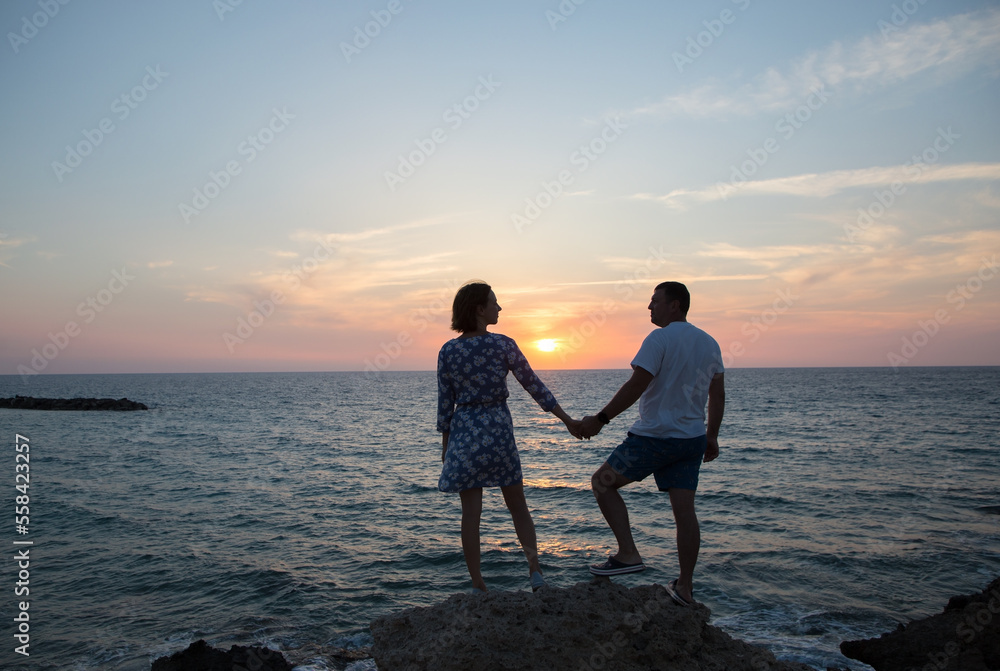 Obraz premium man and woman, he and she in full growth, silhouettes of couple in love against backdrop of sea and sunset stand holding hands. enjoyment of moment, tender feelings, pleasant pastime. Valentine's Day