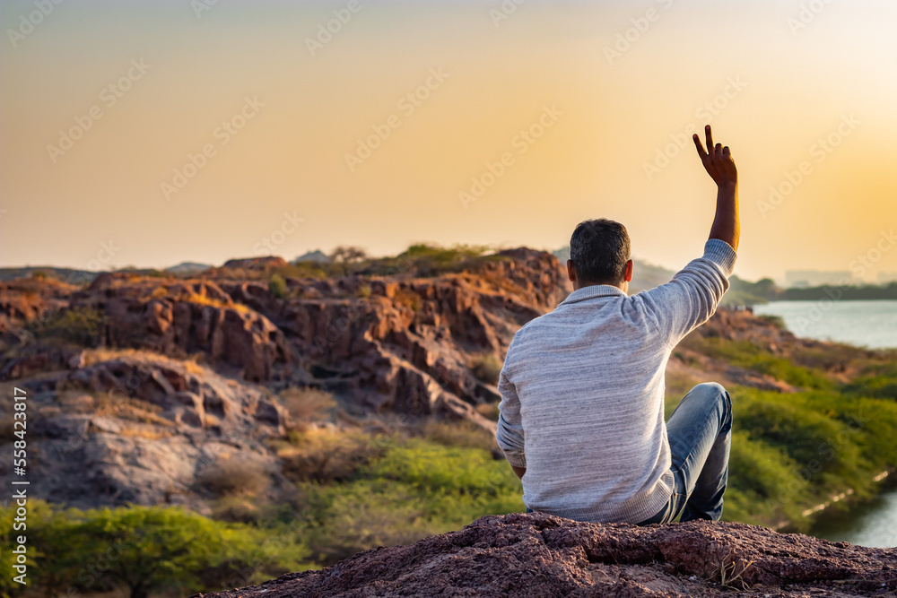 isolated young man sitting at mountain top with lake view and dramatic sky from flat angle