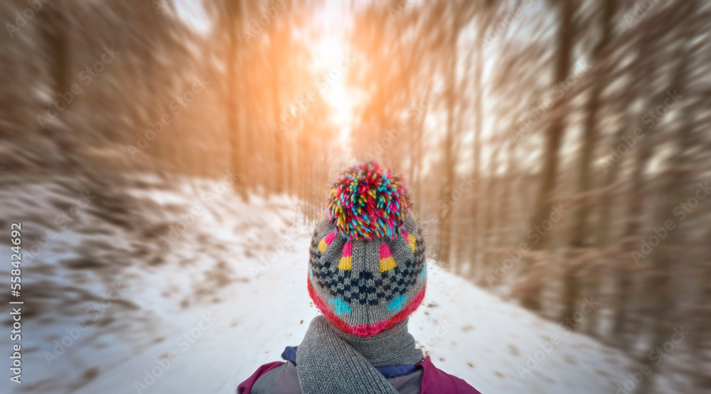 young woman with colorful wool hat hiking in a snowy winter forest
