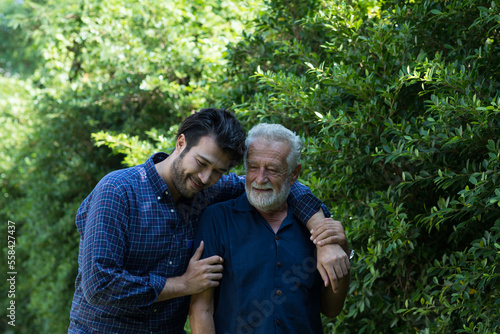 Happy senior father and adult son embracing and talking outdoor garden. Two happy men spending time together in the park. Happy family, holiday and people concept