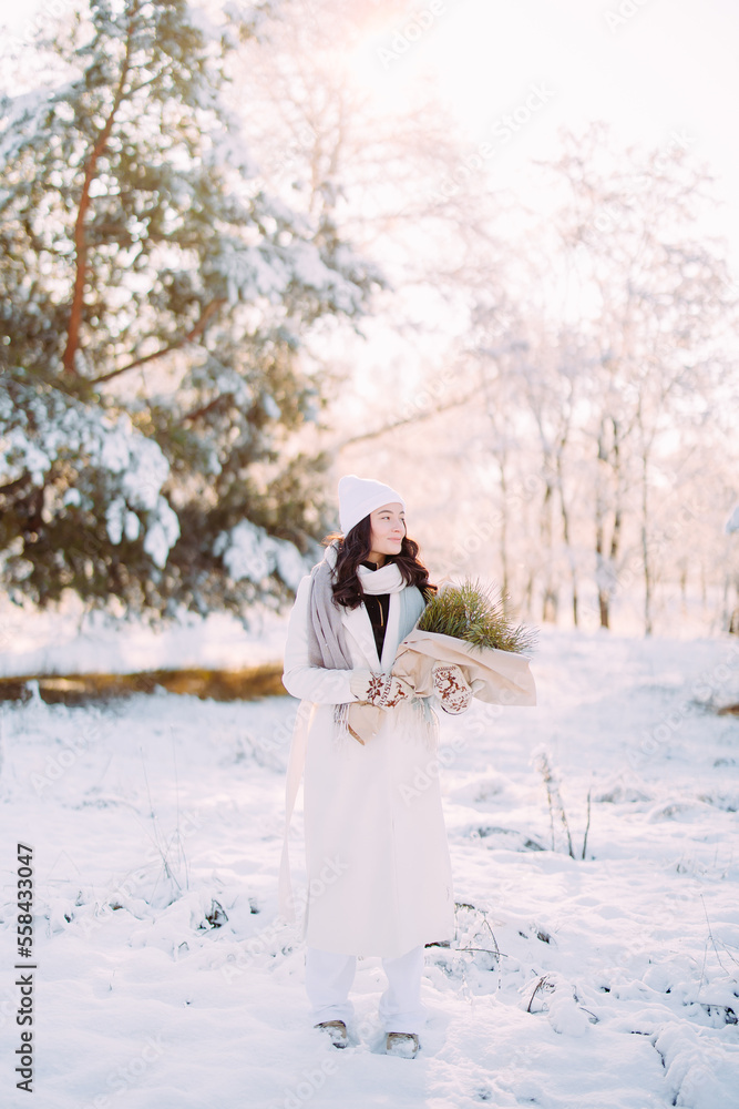 Happy young woman walks in winter forest among pine trees in sunny day.