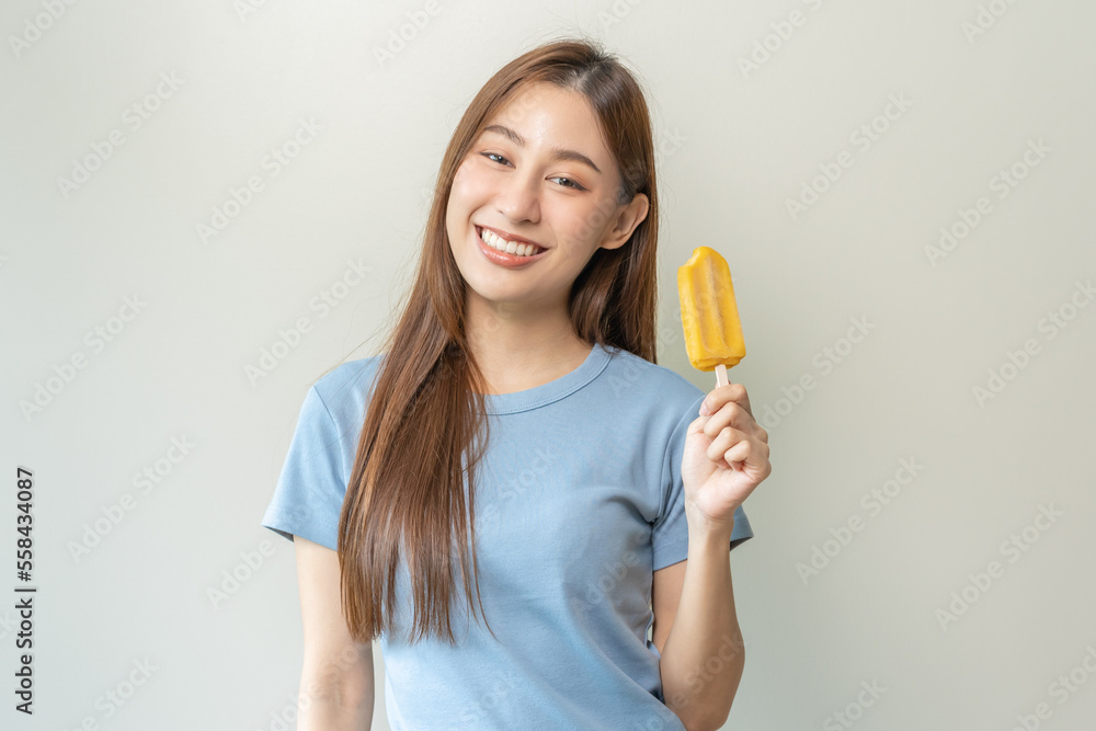 Cheerful enjoy, happy cute asian woman wearing casual with brunette hair, eating popsicle, teenage girl holding ice pop, lolly frozen stick with mango yellow, passion fruit ice cream tasty in summer. Cheerful enjoy, happy cute asian woman wearing casual with brunette hair, eating popsicle, teenage girl holding ice pop, lolly frozen stick with mango yellow, passion fruit ice cream tasty in summer.