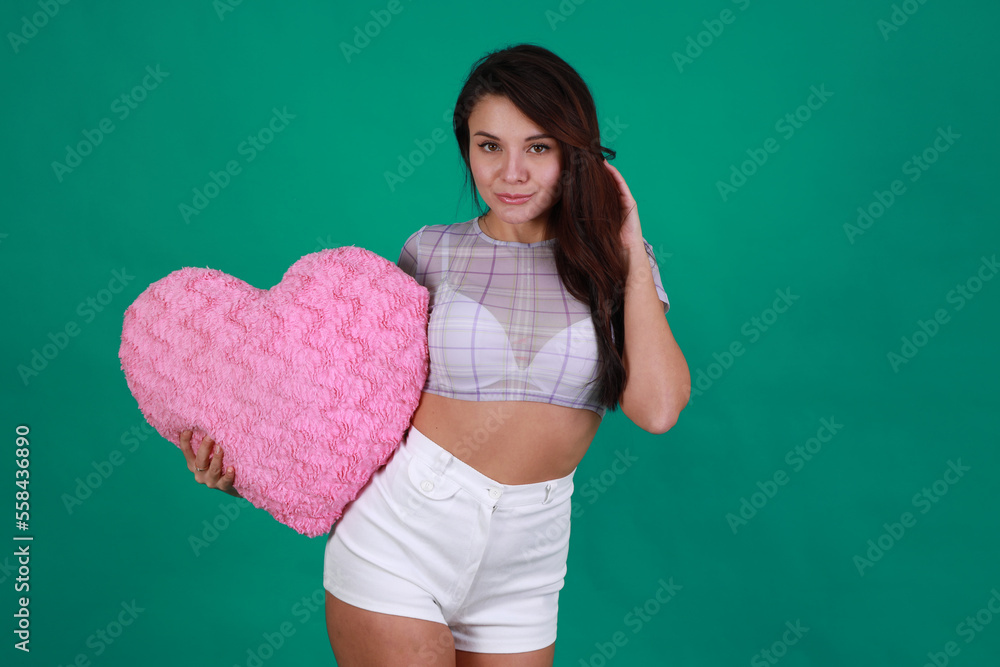 Beautiful young brunette woman holding a heart on green background Beautiful young brunette woman holding a heart on green background