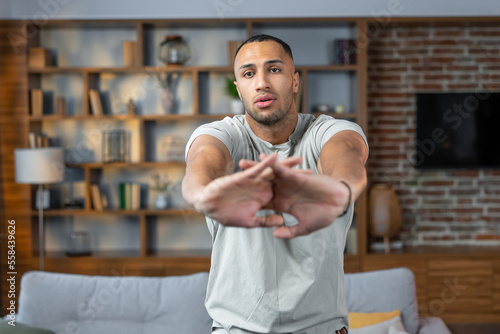 African american  man stretching arms before domestic training, athletic  male warming up his hands during home workout in living room interior