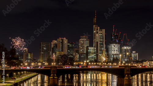 Fototapeta Naklejka Na Ścianę i Meble -  New years eve with fireworks above the skyline of Frankfurt - Main at night at a cold day in winter with colorful reflections in the water.