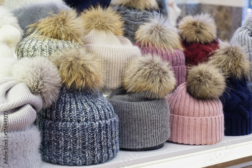 Showcase of trade tent with variety of women's hats for the autumn and winter seasons - hats with fur pom-poms. Small and medium-sized clothing business, product demonstration, seasonal sales.
