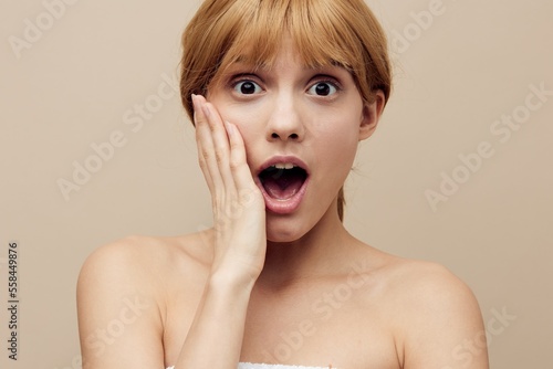 a close horizontal photo with an empty space of a shocked, surprised woman with perfect skin, standing on a background with her hands near her face with her mouth wide open