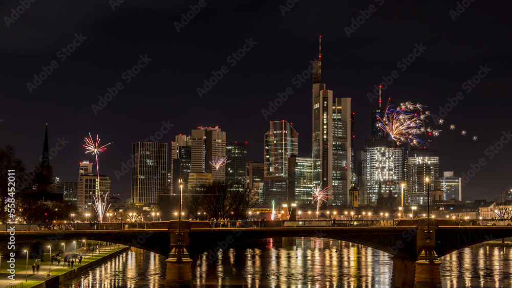Naklejka premium New years eve with fireworks above the skyline of Frankfurt - Main at night at a cold day in winter with colorful reflections in the water.