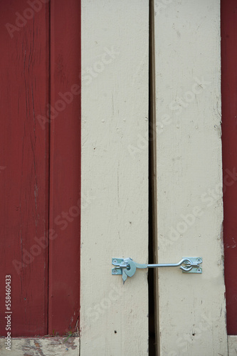 close up of silver door latch on barn door red and white or cream colored barn door with silver or grey hook latch with silver screws to keep barn door closed vertical lines vertical format type space