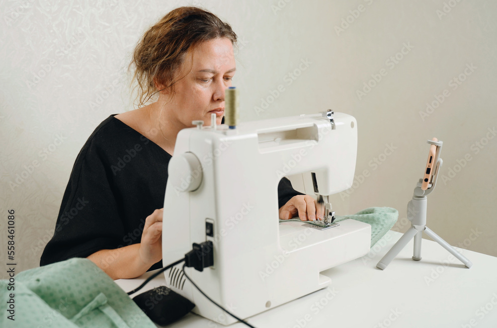 A female seamstress sews green fabric items on a sewing machine.