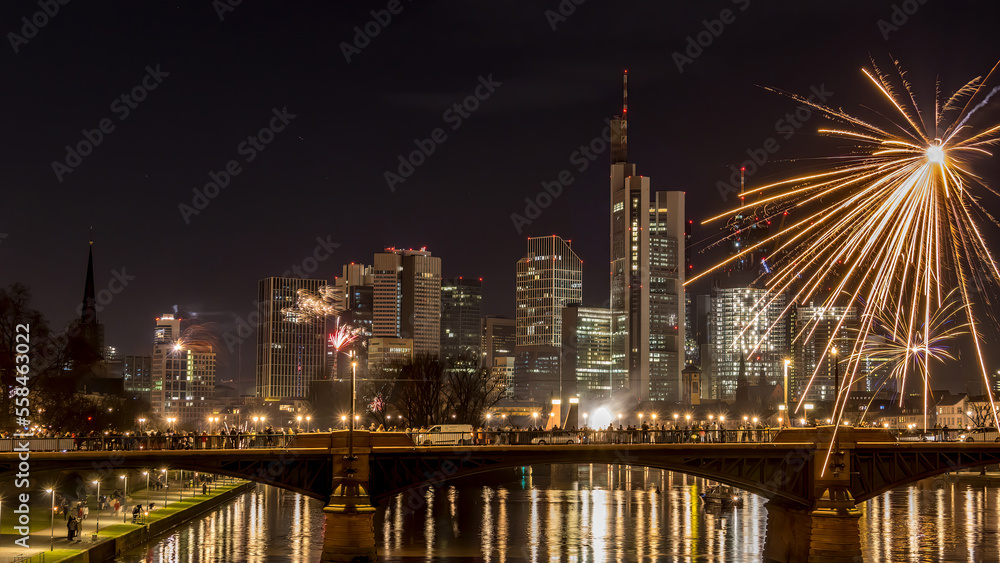 New years eve with fireworks above the skyline of Frankfurt - Main at night at a cold day in winter with colorful reflections in the water.