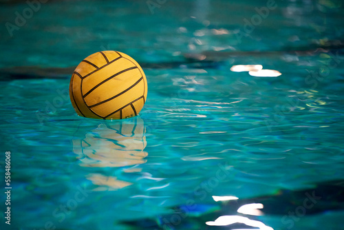 Yellow water polo ball in a swimming pool on blue water background. Film noise and gain