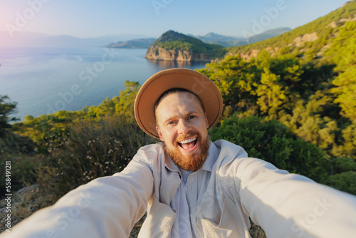 Concept Turkey trip travel on lycian way. Young happy man in hat traveler making selfie photo blue sea with sunset