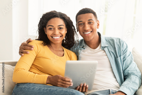 Cheerful millennial african american man and woman surfing in internet, have meeting on tablet, look at camera