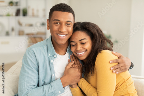Cheerful handsome millennial african american male hugging female, enjoy spare time and looking at camera