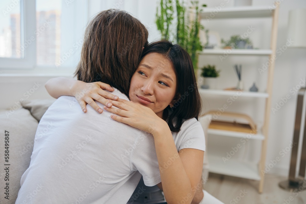 A man hugs his Asian woman friend at home. Psychological support for a friend A man hugs his Asian woman friend at home. Psychological support for a friend