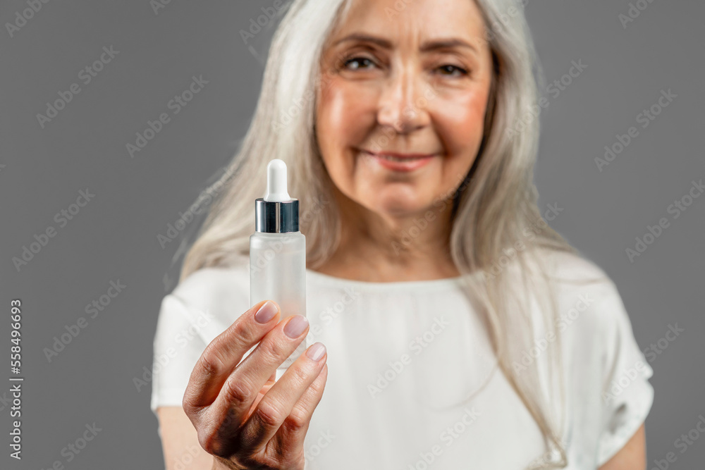 Cheerful pretty mature european lady shows jar of oil or serum for face, recommend anti-wrinkle cosmetic Cheerful pretty mature european lady shows jar of oil or serum for face, recommend anti-wrinkle cosmetic