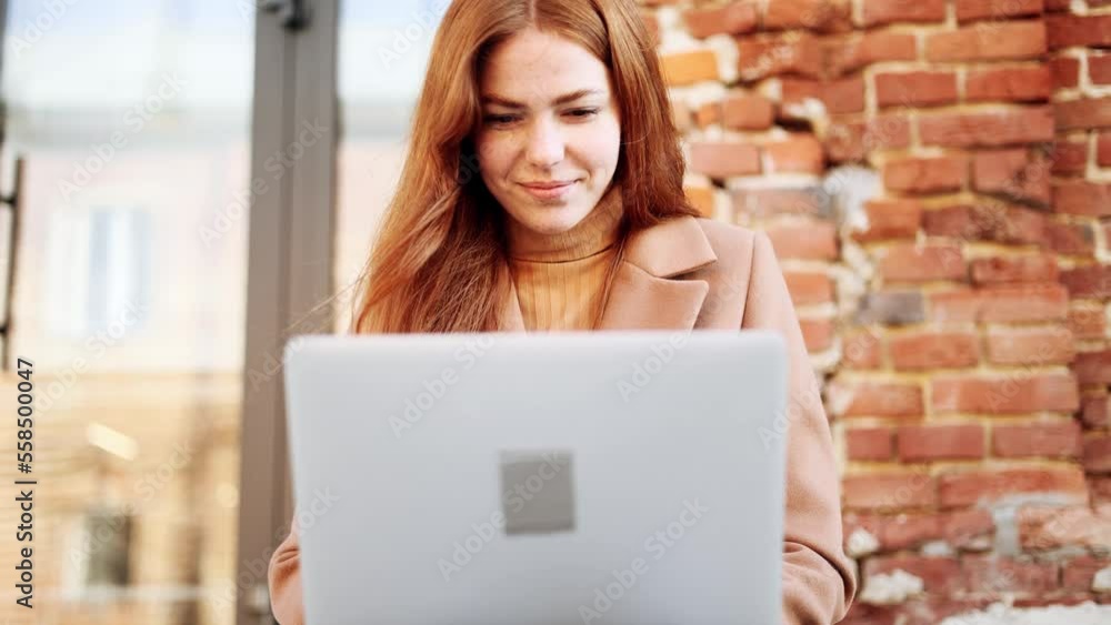 Charming young red haired ginger woman working or studying on laptop sitting on stairs in the urban brick space Busy woman have distance work or online education and looking at the screen outdoors Charming young red haired ginger woman working or studying on laptop sitting on stairs in the urban brick space Busy woman have distance work or online education and looking at the screen outdoors
