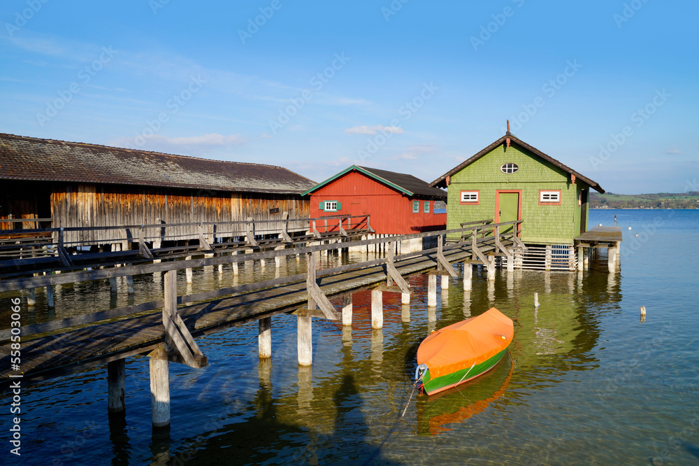 Fototapeta premium a long wooden pier leading to the colorful boat houses on lake Ammersee in the German fishing village Schondorf (Ammersee, Germany) 