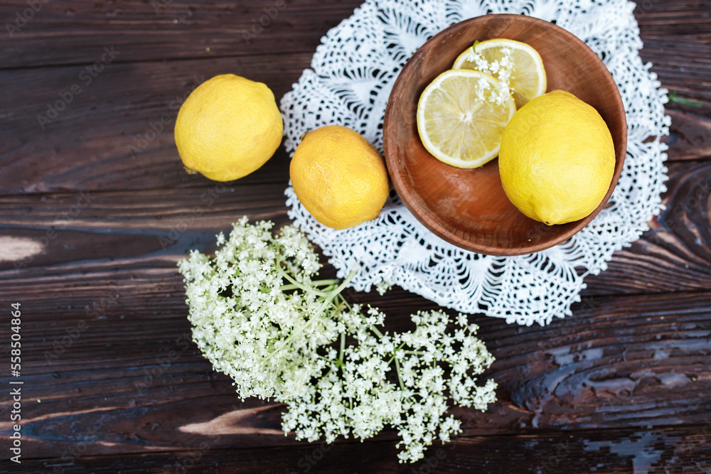 Still life of fresh lemons and elderberry flowers. Ingredients for lemonade and juice from syrup from elderberry flowers. Seasonal summer food. Healing with a healthy diet with ambucus medicines