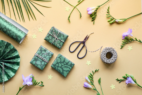 Spring flowers and gift boxes. Golden yellow paper background with green wrapping paper, presents, scissors and cord. Flat lay, top view with freesia and tulips. Orange, green, purple pastel colors.