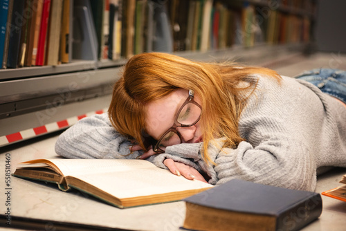 Teen girl with red hair and glasses sleeping while studying.