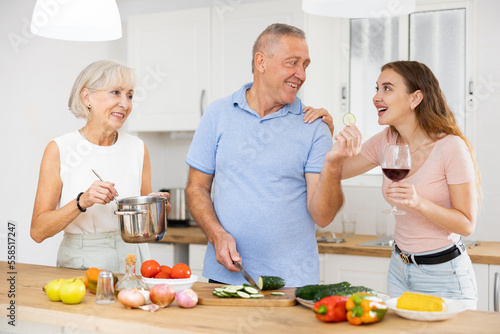 Positive senior couple spending time together with their adult daughter, cooking delicious meals for dinner