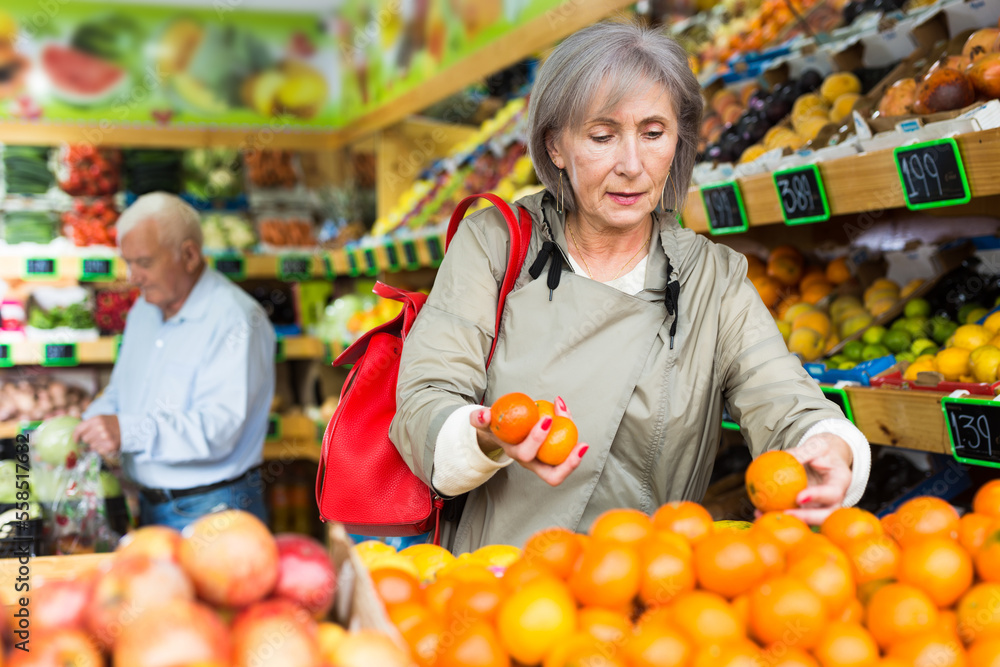 Mature woman selecting tangerines in supermarket. Senior man shopping in background.