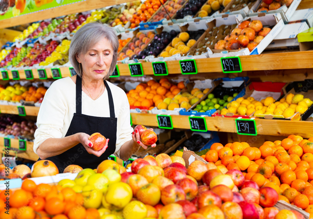 Female supermarket worker stacking fruits on shelf in salesroom