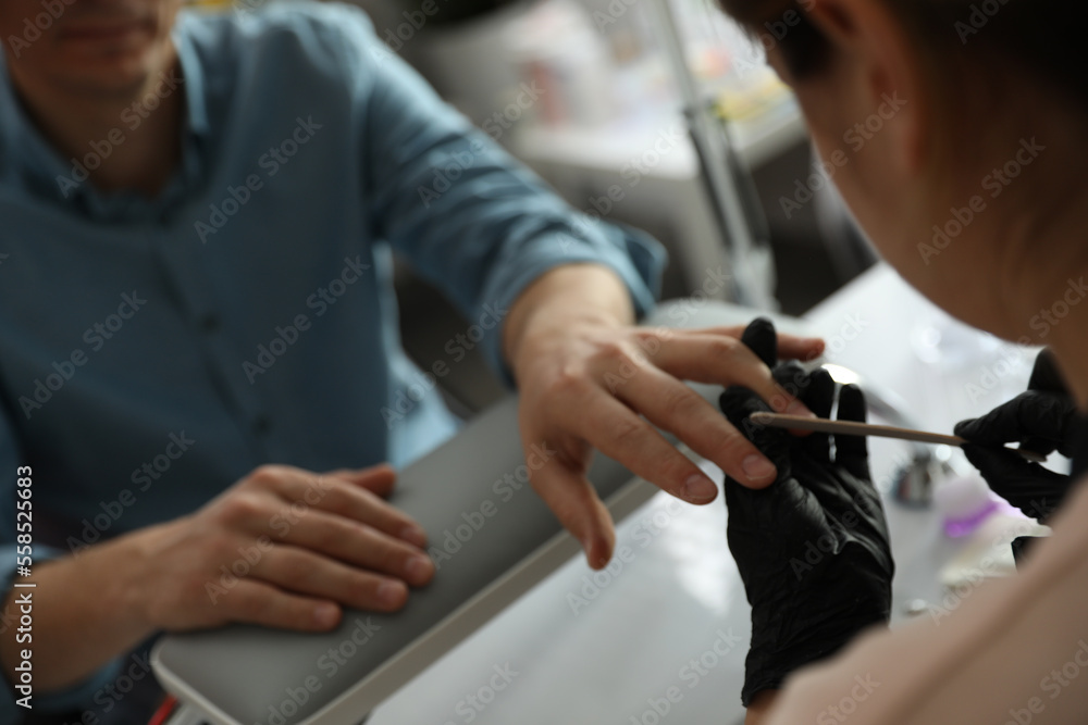 Professional manicurist filing client's nails in beauty salon, closeup Professional manicurist filing client's nails in beauty salon, closeup