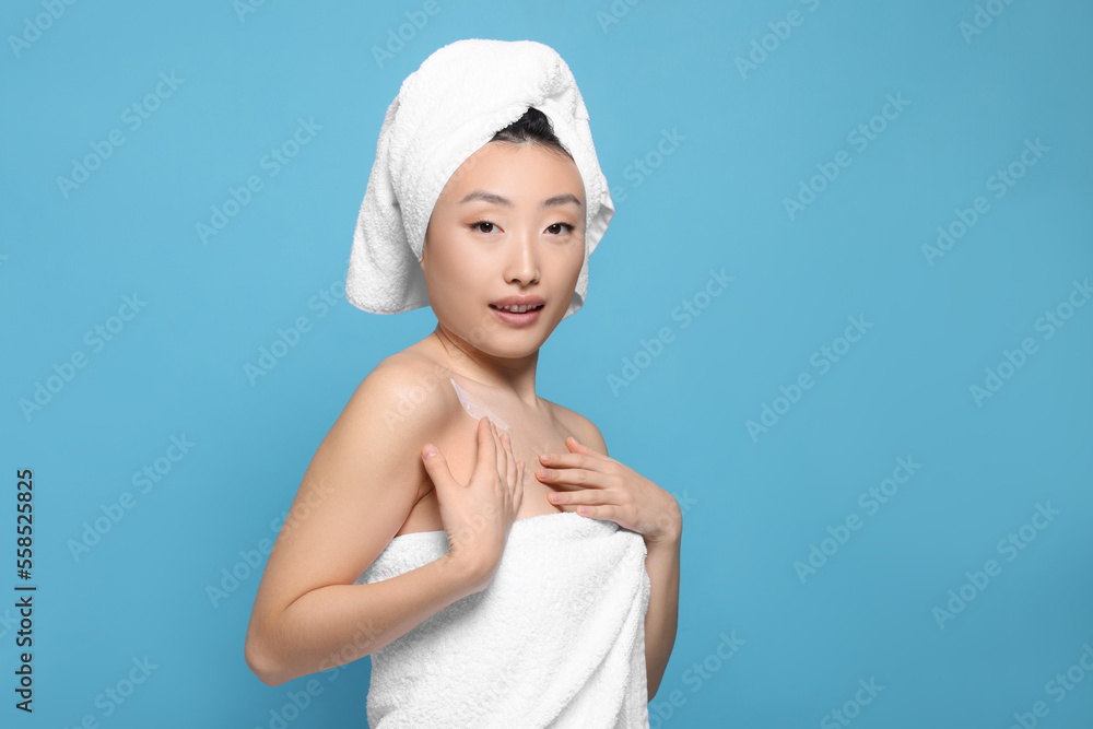 Beautiful young Asian woman applying body cream onto shoulder on light blue background, space for text Beautiful young Asian woman applying body cream onto shoulder on light blue background, space for text