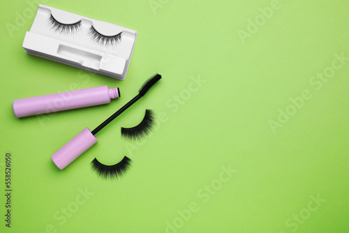 Flat lay composition with fake eyelashes and mascara brush on green background. Space for text