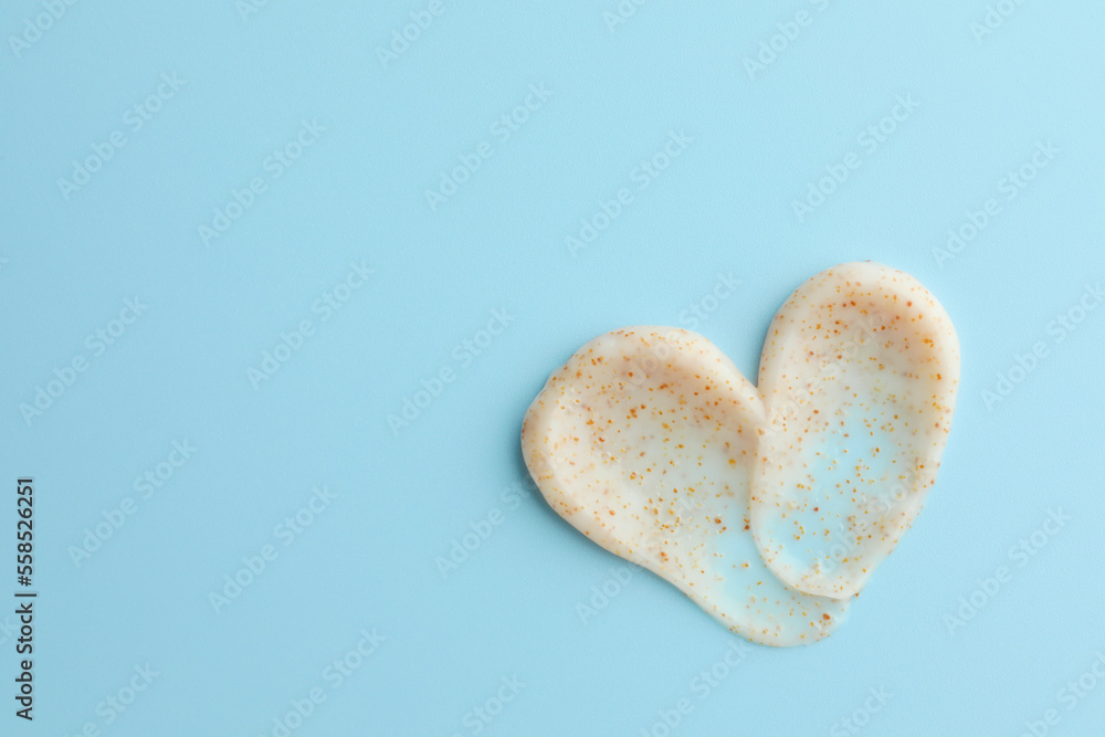 Fototapeta premium Samples of face scrub in shape of heart on light blue background, top view. Space for text