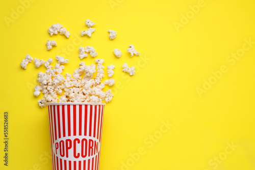 Fototapeta Naklejka Na Ścianę i Meble -  Overturned paper cup with delicious popcorn on yellow background, flat lay. Space for text