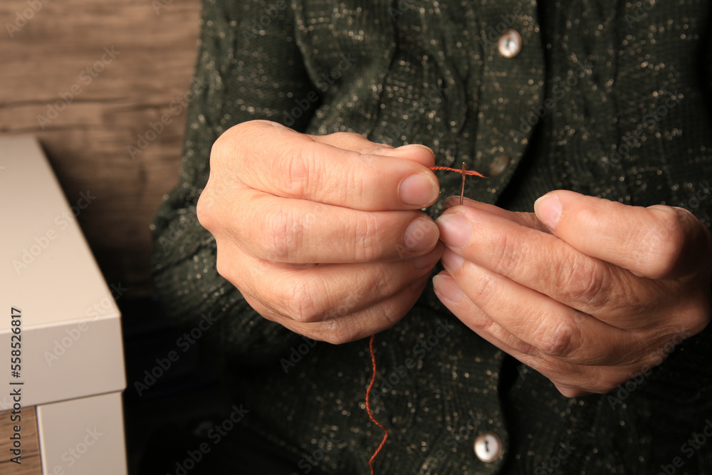 Fototapeta premium Closeup view of woman threading needle indoors. Sewing equipment