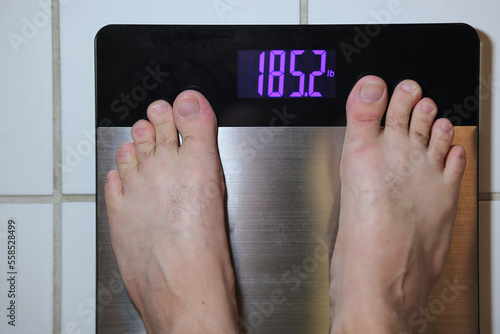 Stainless steel digital scale with mans feet weighing 185 pounds on tile floor photo