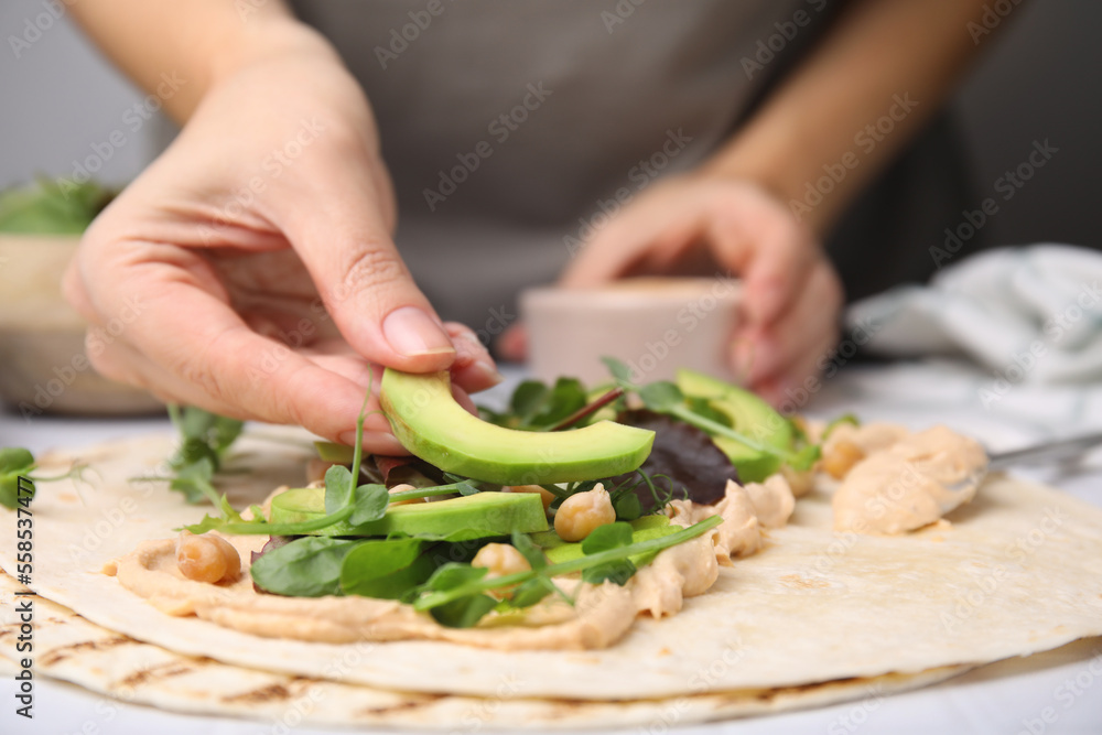 Woman making delicious hummus wrap with vegetables at table, closeup Woman making delicious hummus wrap with vegetables at table, closeup