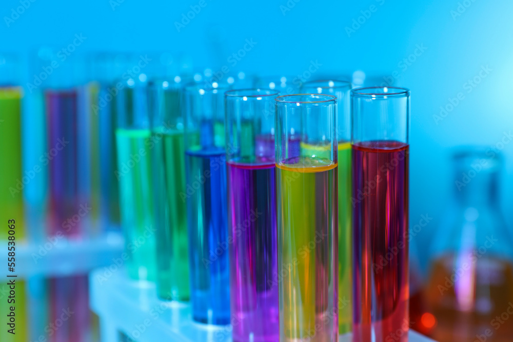 Many test tubes with colorful liquids on light blue background, closeup Many test tubes with colorful liquids on light blue background, closeup