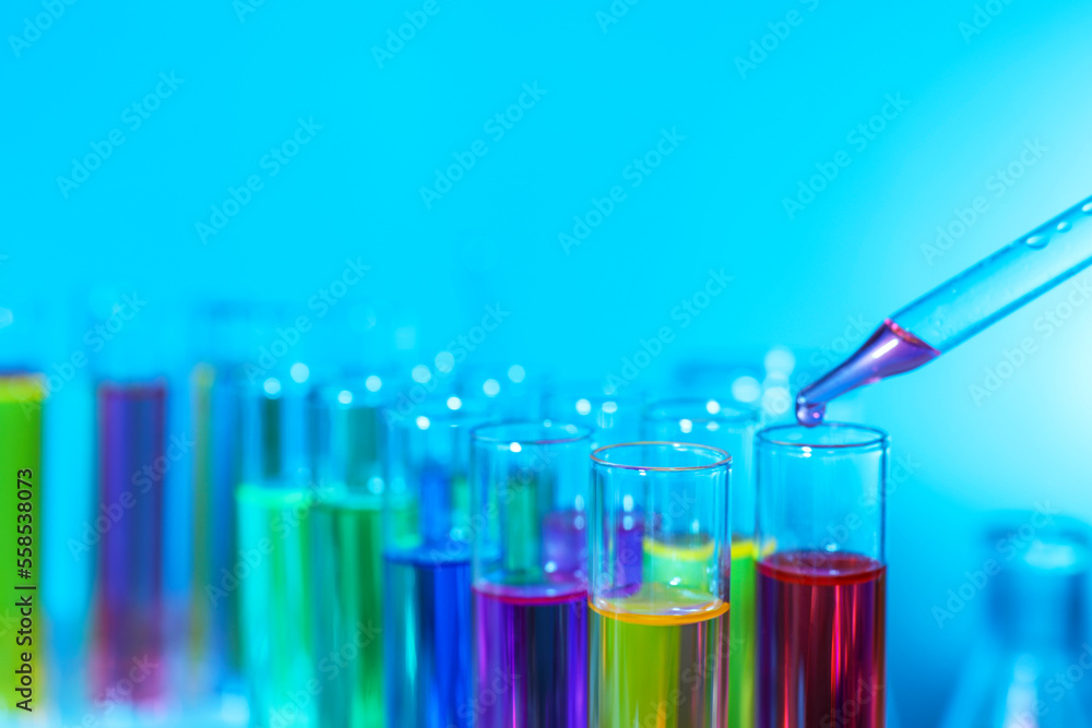 Dripping liquid from pipette into test tube on light blue background, closeup Dripping liquid from pipette into test tube on light blue background, closeup